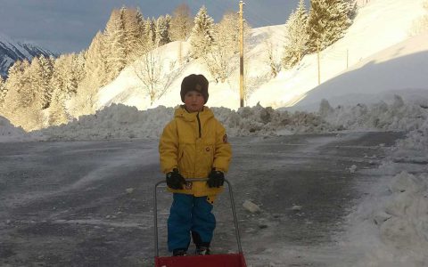 Kind schiebt Schnee auf verschneitem Kinderbauernhof Steffenegg, Winterurlaub für Familien