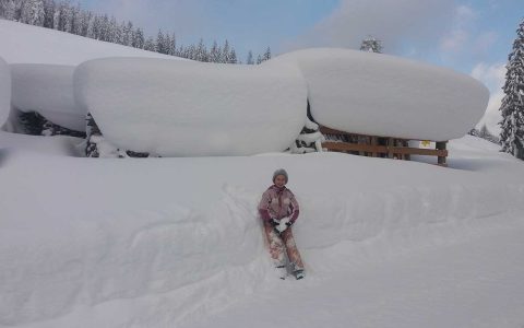 Kind spielt im Schnee vor tief verschneitem Bauernhof Steffenegg, Familienurlaub Österreich Natur