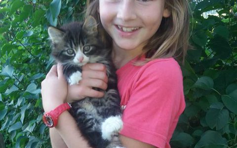 Lächelndes Mädchen hält Bauernhofkätzchen, Kinderbauernhof Steffenegg, Familienurlaub Natur