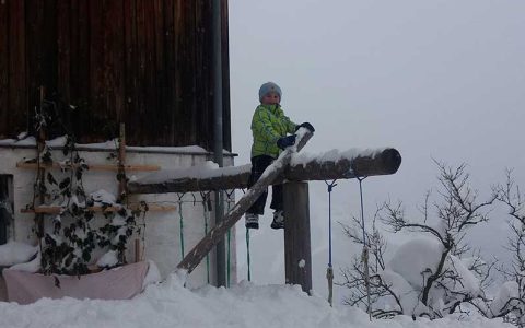 Kind mit Winterkleidung vor verschneitem Bauernhof Steffenegg, Familienurlaub in Österreich